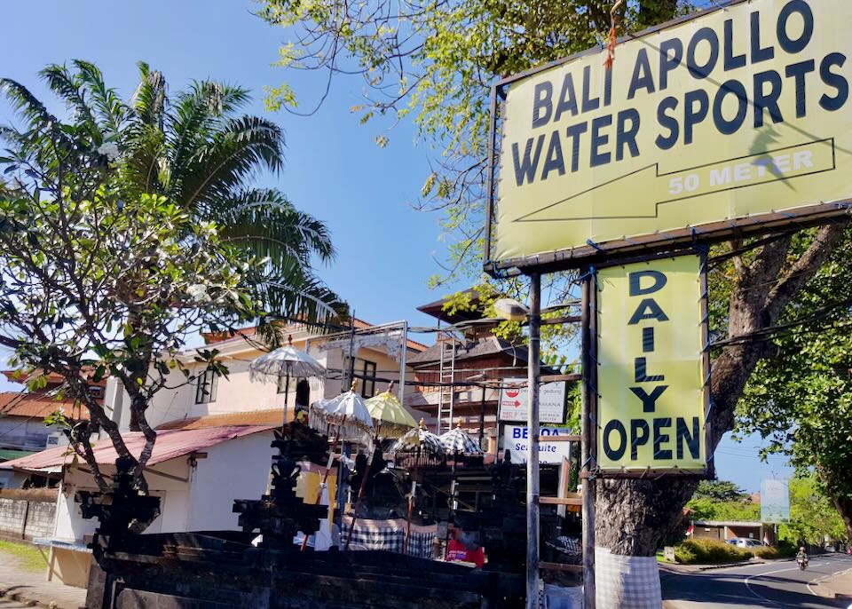 A light yellow sun-bleached sign says, Bali Apollo Water Sports.