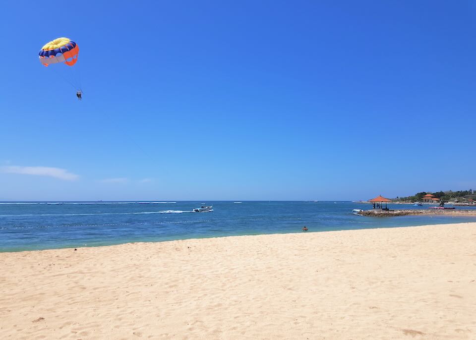 A person parasails over the water at the beach.