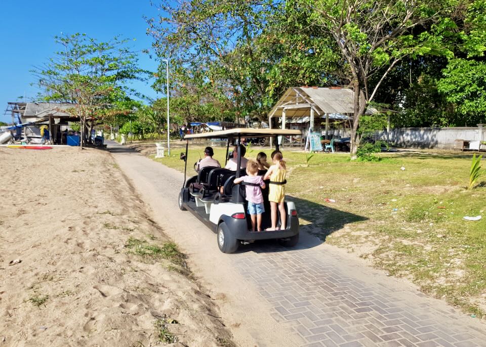 Two children and their parents ride on a golf cart.