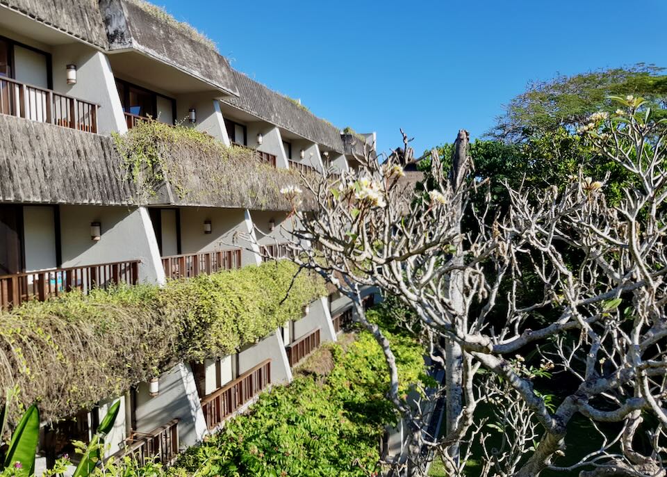 The outside of the hotel shows three levels of balconies overlooking the gardens.