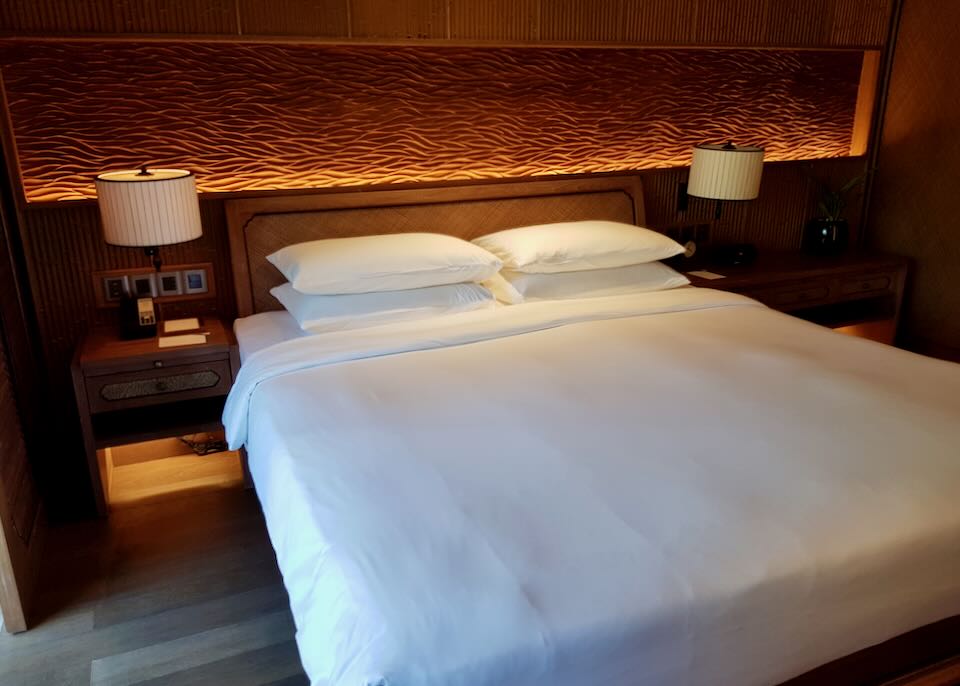 A wood-carved headboard is low-lit above the bed in the hotel room.