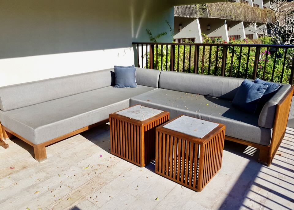 An outdoor sofa sectional sits in the sun on a wood deck.