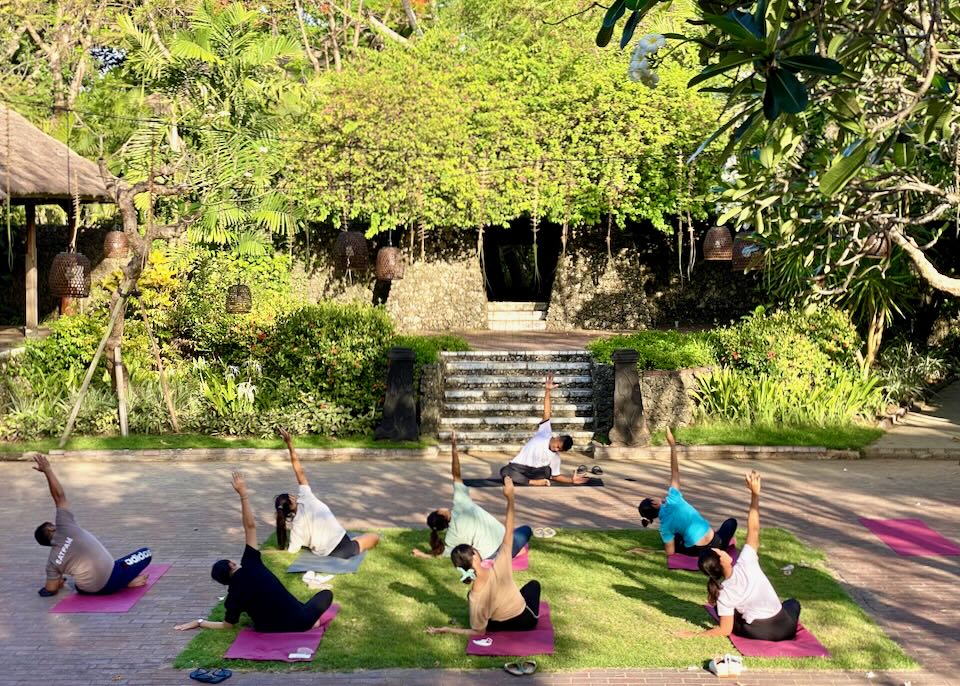 Guests sit on bright pink yoga mats and stretch during a outside class.