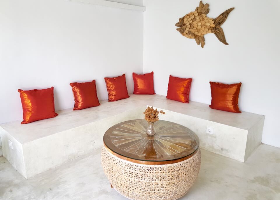 A white marble bench with orange back cushions sits along a wall.