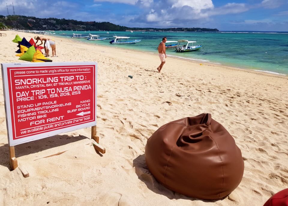 A bean bag sits on the beach next to a rental sign.