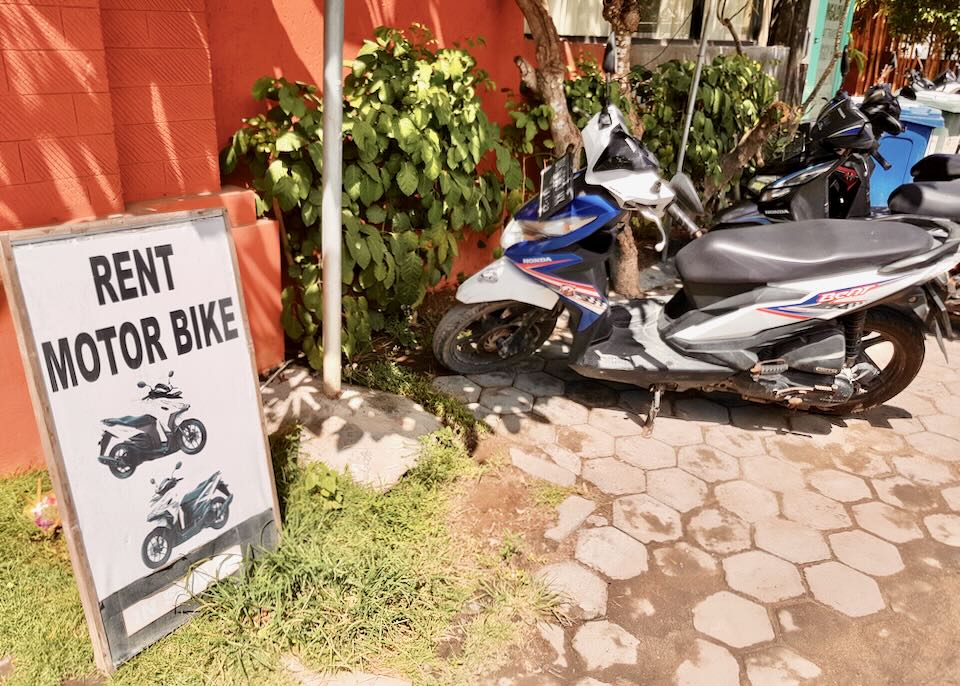 A motorcycles sit in a row next to a "Rent Motor Bike" sign.