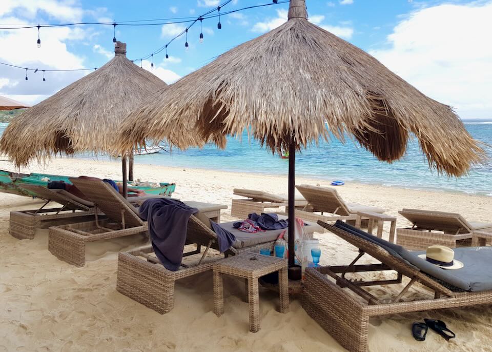 Two thatched umbrellas cover lounge chairs on the beach.