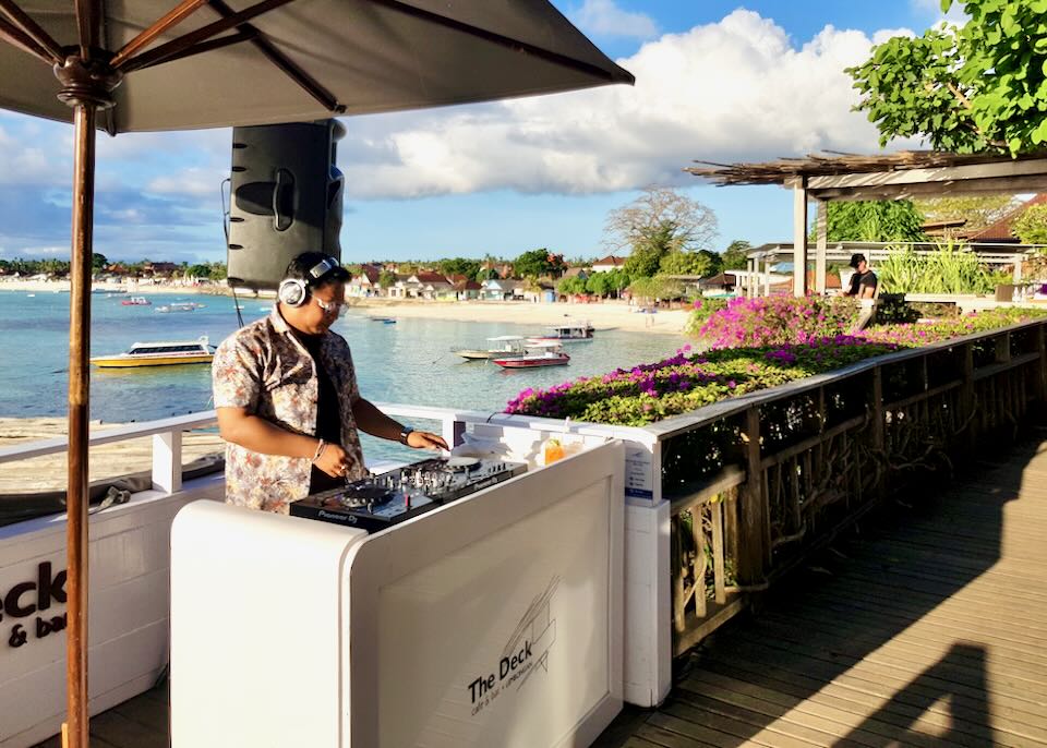 A DJ mixes on a board on the balcony over the ocean.