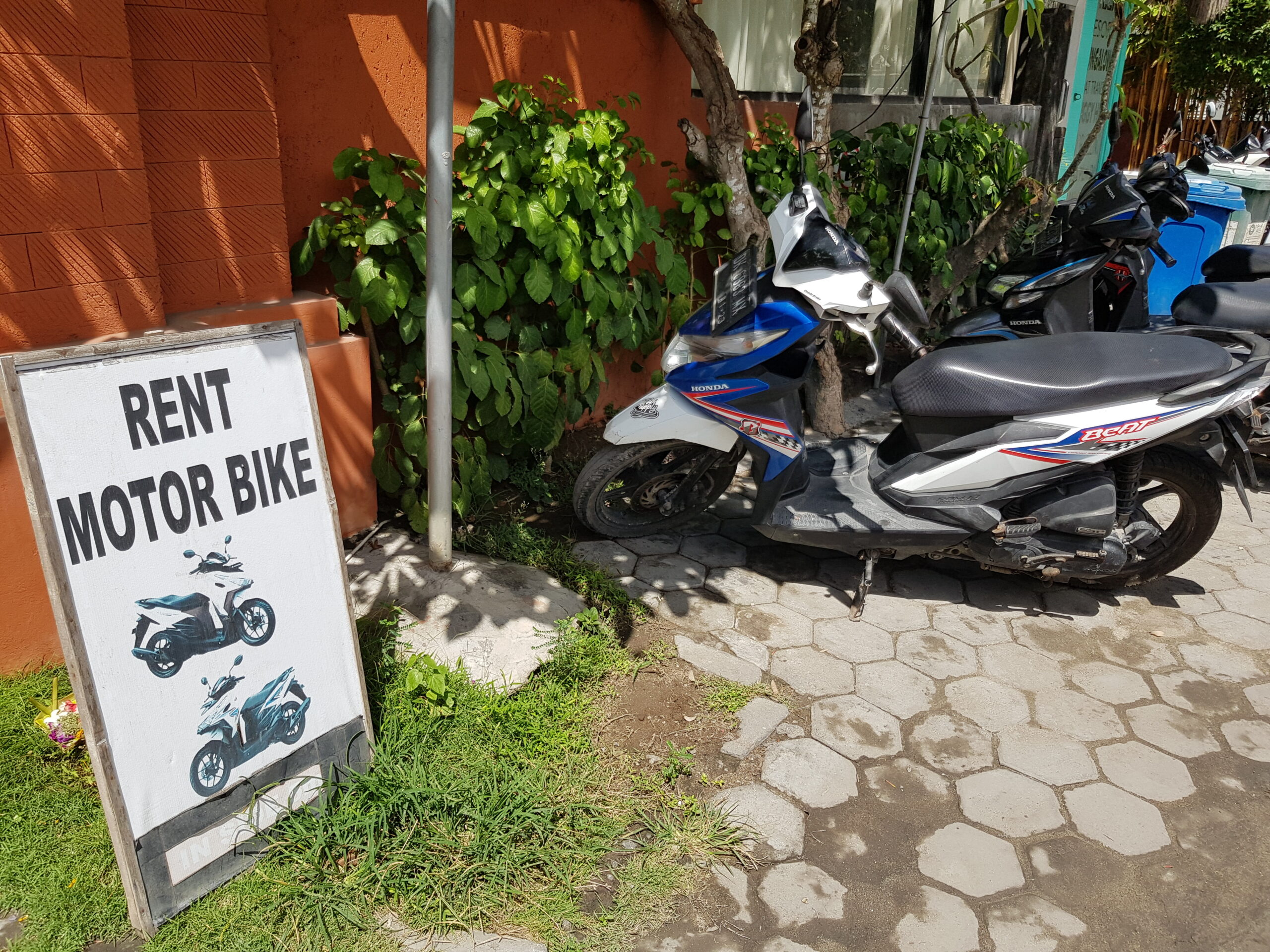 A motorcycle is parked next to a Rent Motor Bike sign.