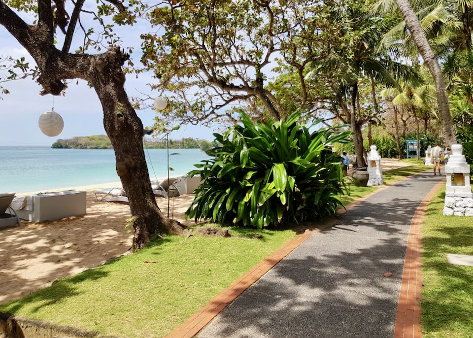 A paved path surrounded by lawns and the beach on one side.