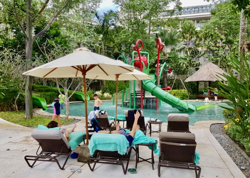 Families watch their kids play in the children's pool at Mövenpick Resort & Spa Jimbaran Bali.